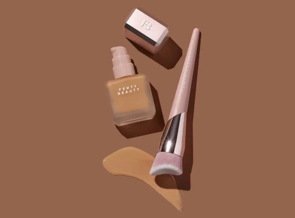 A close-up Fenty Beauty foundation bottle beside a sculptural array of bottles in a range of skin-tone shades.